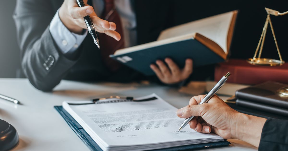 Attorney with law book and another with hand signing a contract.